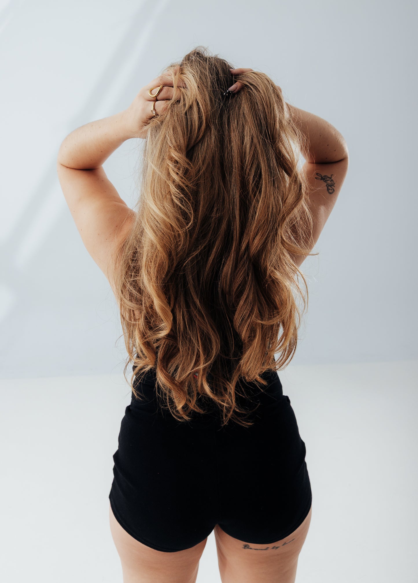 Person with long blonde hair and tattoos on a plain background wearing a cute black set